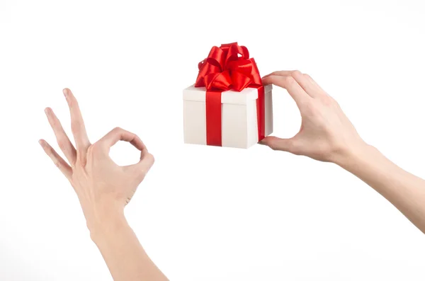 Het thema van vieringen en giften: hand met een geschenk verpakt in witte doos met rood lint en boog, het mooiste geschenk geïsoleerd op een witte achtergrond in studio — Stockfoto