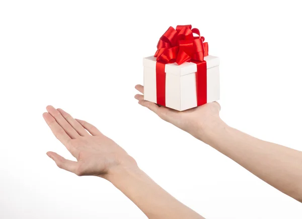 El tema de las celebraciones y regalos: la mano sosteniendo un regalo envuelto en caja blanca con cinta roja y lazo, el regalo más hermoso aislado sobre fondo blanco en el estudio —  Fotos de Stock