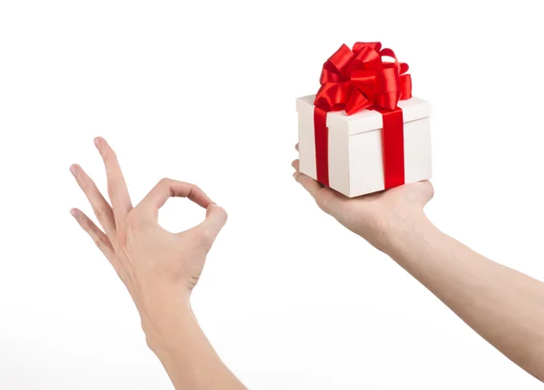 Het thema van vieringen en giften: hand met een geschenk verpakt in witte doos met rood lint en boog, het mooiste geschenk geïsoleerd op een witte achtergrond in studio — Stockfoto