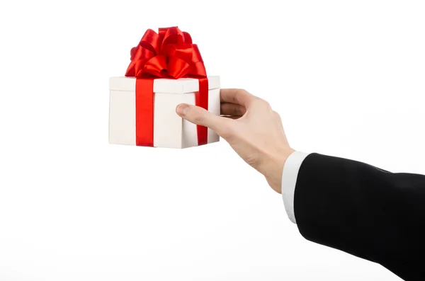 The theme of celebrations and gifts: a man in a black suit holding a exclusive gift wrapped in white box with red ribbon and bow, the most beautiful gift isolated on white background in studio — Stock Photo, Image