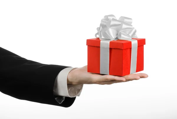 El tema de las celebraciones y regalos: un hombre en un traje negro con un regalo exclusivo envuelto en caja roja con cinta blanca y lazo, el regalo más hermoso aislado sobre fondo blanco en el estudio — Foto de Stock