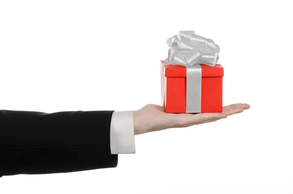 Il tema delle celebrazioni e dei regali: un uomo in abito nero con in mano un regalo esclusivo avvolto in scatola rossa con nastro bianco e fiocco, il regalo più bello isolato su sfondo bianco in studio — Foto Stock