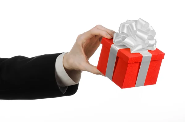 The theme of celebrations and gifts: a man in a black suit holding a exclusive gift wrapped in red box with white ribbon and bow, the most beautiful gift isolated on white background in studio — Stock Photo, Image