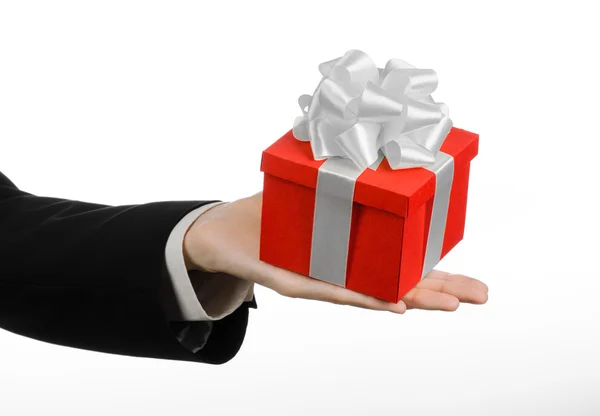 Le thème des célébrations et des cadeaux : un homme en costume noir tenant un cadeau exclusif enveloppé dans une boîte rouge avec ruban blanc et arc, le plus beau cadeau isolé sur fond blanc en studio — Photo