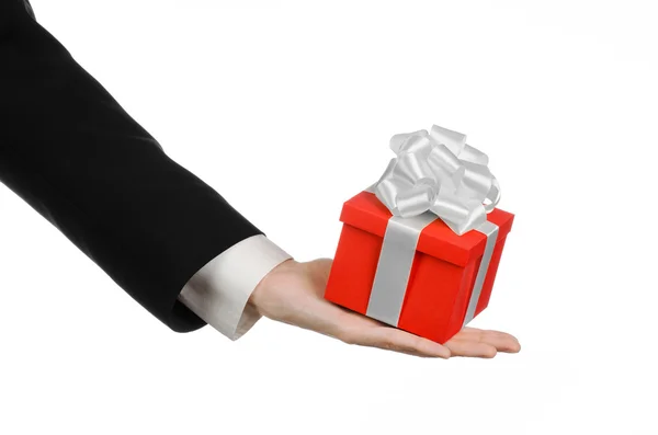 The theme of celebrations and gifts: a man in a black suit holding a exclusive gift wrapped in red box with white ribbon and bow, the most beautiful gift isolated on white background in studio — Stock Photo, Image