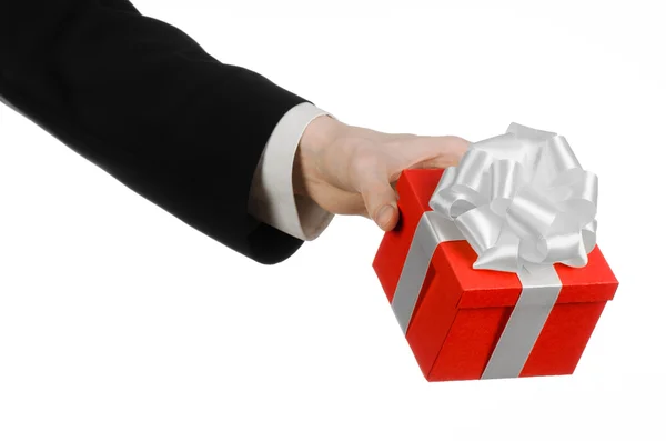 El tema de las celebraciones y regalos: un hombre en un traje negro con un regalo exclusivo envuelto en caja roja con cinta blanca y lazo, el regalo más hermoso aislado sobre fondo blanco en el estudio — Foto de Stock