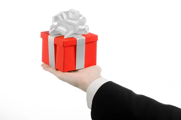 Le thème des célébrations et des cadeaux : un homme en costume noir tenant un cadeau exclusif enveloppé dans une boîte rouge avec ruban blanc et arc, le plus beau cadeau isolé sur fond blanc en studio — Photo