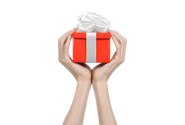 El tema de las celebraciones y regalos: la mano sosteniendo un regalo envuelto en caja roja con cinta blanca y lazo, el regalo más hermoso aislado sobre fondo blanco en el estudio — Foto de Stock