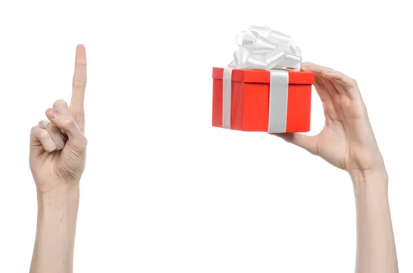 Het thema van vieringen en giften: hand met een geschenk verpakt in rode doos met wit lint en boog, het mooiste geschenk geïsoleerd op een witte achtergrond in studio — Stockfoto