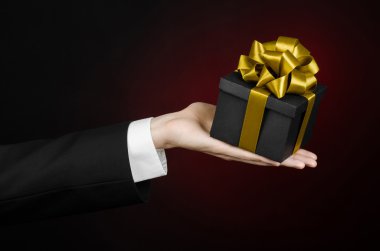 Kutlamalar ve hediye Tema: holding özel hediye altın şerit, güzel bir kara kutu ambalajlı ve pahalı hediye izole Studio koyu kırmızı zemin üzerine siyah takım elbiseli bir adam