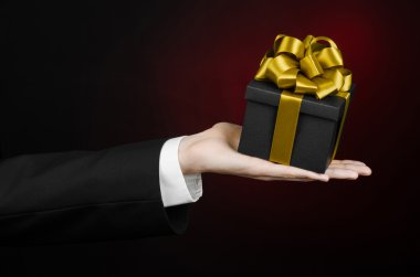 Kutlamalar ve hediye Tema: holding özel hediye altın şerit, güzel bir kara kutu ambalajlı ve pahalı hediye izole Studio koyu kırmızı zemin üzerine siyah takım elbiseli bir adam