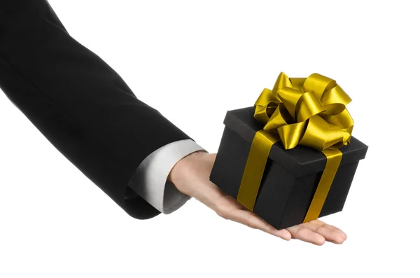 The theme of celebrations and gifts: a man in a black suit holding a exclusive gift packaged in a black box with gold ribbon and bow, the most beautiful gift isolated on white background in studio — Stock Photo, Image