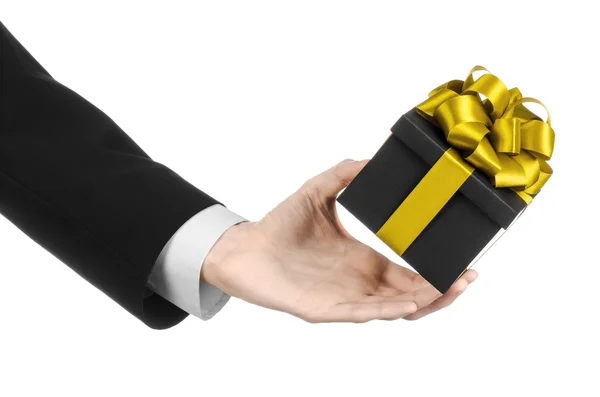 The theme of celebrations and gifts: a man in a black suit holding a exclusive gift packaged in a black box with gold ribbon and bow, the most beautiful gift isolated on white background in studio — Stock Photo, Image