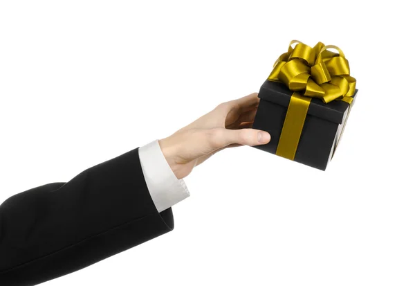 The theme of celebrations and gifts: a man in a black suit holding a exclusive gift packaged in a black box with gold ribbon and bow, the most beautiful gift isolated on white background in studio — Stock Photo, Image