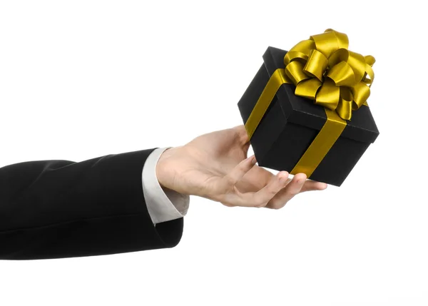 The theme of celebrations and gifts: a man in a black suit holding a exclusive gift packaged in a black box with gold ribbon and bow, the most beautiful gift isolated on white background in studio — Stock Photo, Image