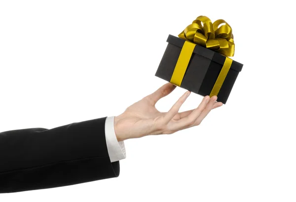 庆祝活动和礼品的主题: 一个穿着一套黑色的西装，持有专属礼品包装在一个黑箱与金丝带和蝴蝶结，孤立在工作室中的白色背景上的最美的礼物 — 图库照片