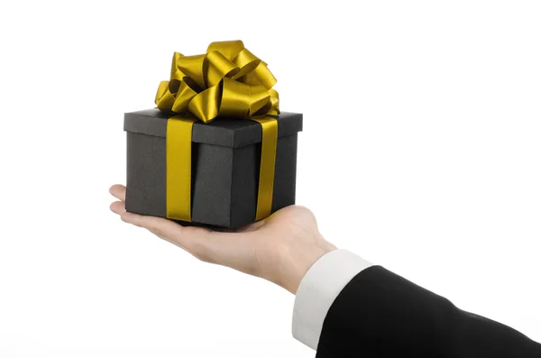 The theme of celebrations and gifts: a man in a black suit holding a exclusive gift packaged in a black box with gold ribbon and bow, the most beautiful gift isolated on white background in studio — Stock Photo, Image