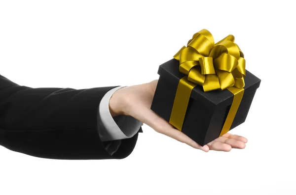 Le thème des célébrations et des cadeaux : un homme en costume noir tenant un cadeau exclusif emballé dans une boîte noire avec ruban d'or et arc, le plus beau cadeau isolé sur fond blanc en studio — Photo