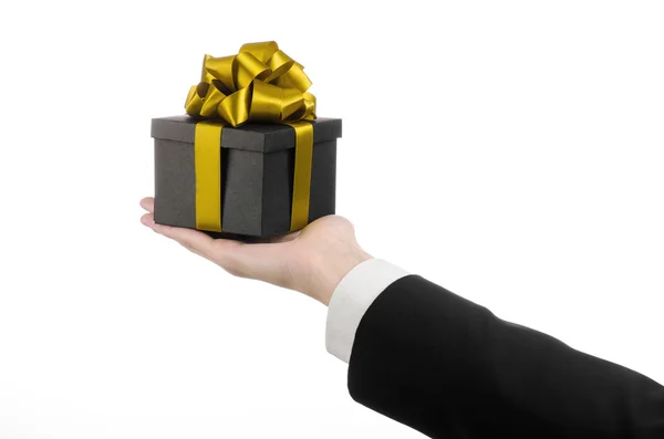 The theme of celebrations and gifts: a man in a black suit holding a exclusive gift packaged in a black box with gold ribbon and bow, the most beautiful gift isolated on white background in studio — Stock Photo, Image