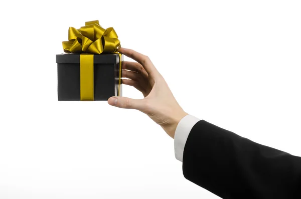 The theme of celebrations and gifts: a man in a black suit holding a exclusive gift packaged in a black box with gold ribbon and bow, the most beautiful gift isolated on white background in studio — Stock Photo, Image