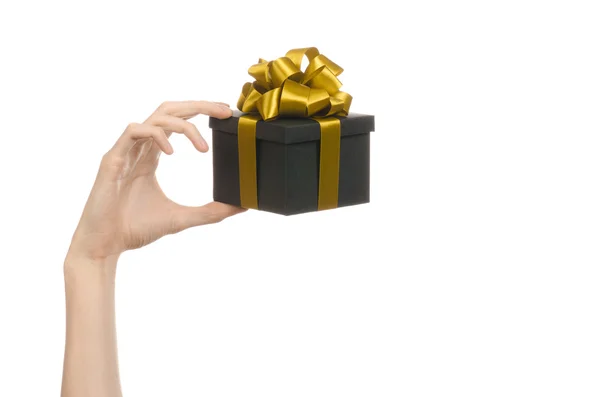 The theme of celebrations and gifts: hand holding a gift wrapped in a black box with gold ribbon and bow, the most beautiful gift isolated on white background in studio — Stock Photo, Image