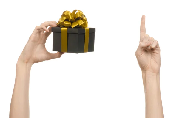 The theme of celebrations and gifts: hand holding a gift wrapped in a black box with gold ribbon and bow, the most beautiful gift isolated on white background in studio — Stock Photo, Image