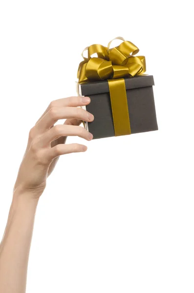 Das Thema der Feiern und Geschenke: Hand hält ein Geschenk in einer schwarzen Schachtel mit goldenem Band und Schleife verpackt, das schönste Geschenk isoliert auf weißem Hintergrund im Studio — Stockfoto