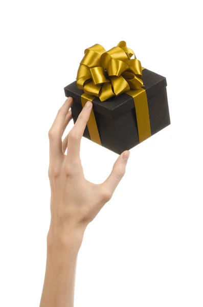 Temat för fester och gåvor: handen håller en gåva insvept i en svart låda med guld band och rosett, den vackraste gåva isolerad på vit bakgrund i studio — Stockfoto