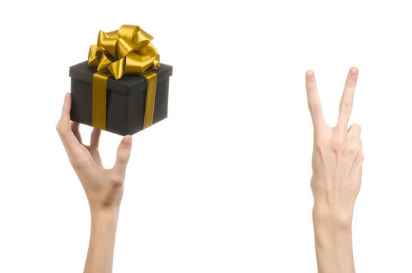 Le thème des célébrations et des cadeaux : main tenant un cadeau enveloppé dans une boîte noire avec ruban d'or et arc, le plus beau cadeau isolé sur fond blanc en studio — Photo