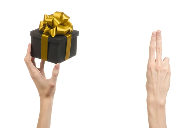 The theme of celebrations and gifts: hand holding a gift wrapped in a black box with gold ribbon and bow, the most beautiful gift isolated on white background in studio — Stock Photo, Image