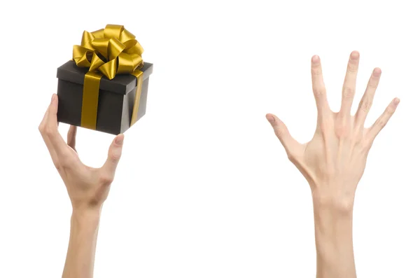El tema de las celebraciones y regalos: la mano sosteniendo un regalo envuelto en una caja negra con cinta de oro y lazo, el regalo más hermoso aislado sobre fondo blanco en el estudio — Foto de Stock