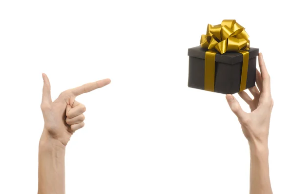 Le thème des célébrations et des cadeaux : main tenant un cadeau enveloppé dans une boîte noire avec ruban d'or et arc, le plus beau cadeau isolé sur fond blanc en studio — Photo