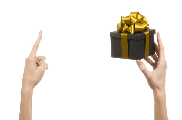 Het thema van vieringen en giften: hand met een geschenk verpakt in een zwarte doos met gouden lint en boog, het mooiste geschenk geïsoleerd op een witte achtergrond in studio — Stockfoto