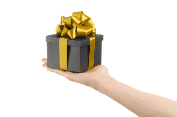 Het thema van vieringen en giften: hand met een geschenk verpakt in een zwarte doos met gouden lint en boog, het mooiste geschenk geïsoleerd op een witte achtergrond in studio — Stockfoto