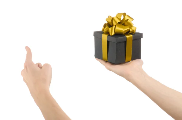 Na temat uroczystości i prezenty: ręka trzyma prezent owinięty w czarne pudełko z złota wstążka i łuk, Najpiękniejszy prezent na białym tle na białym tle w studio — Zdjęcie stockowe