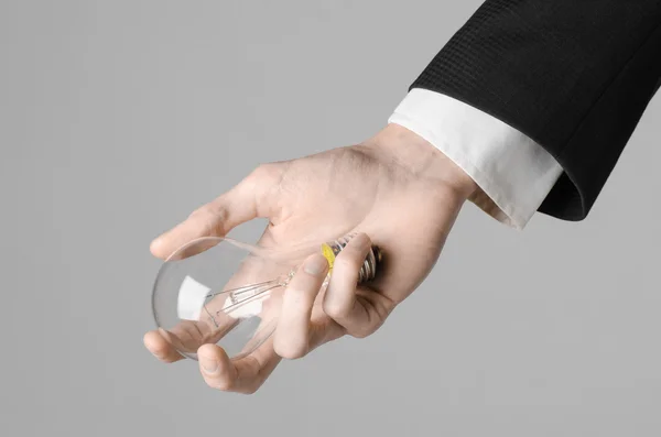 Consumptie en nieuwe business idee thema: man's hand in een zwart pak een gloeilamp houden op een grijze achtergrond in studio — Stockfoto