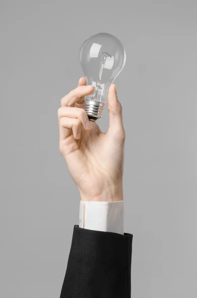 Consumo de energía y nuevo tema de la idea de negocio: la mano del hombre en un traje negro con una bombilla sobre un fondo gris en el estudio — Foto de Stock