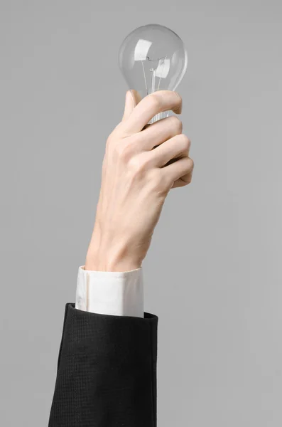 Consumptie en nieuwe business idee thema: man's hand in een zwart pak een gloeilamp houden op een grijze achtergrond in studio — Stockfoto