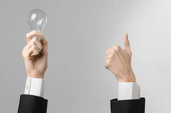 Consumo de energia e novo tema de ideia de negócio: mão do homem em um terno preto segurando uma lâmpada em um fundo cinza no estúdio — Fotografia de Stock