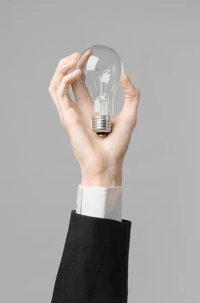 电力消费和新的商业思想主题: 人的手中持有一个灯泡在工作室中的灰色背景上的黑色西装 — 图库照片
