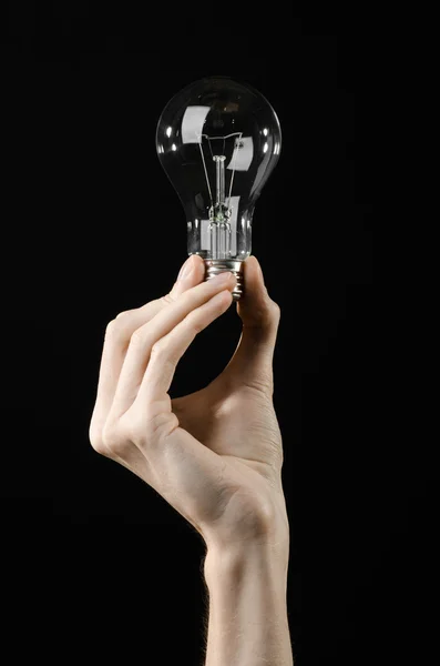 Energy consumption and energy saving topic: human hand holding a light bulb on black background in studio — Stock Photo, Image