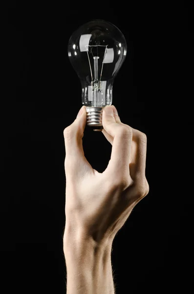 Энергопотребление и энергосбережение: рука человека держит лампочку на черном фоне в студии — стоковое фото