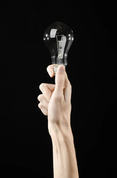 Consumo de energía y ahorro de energía: mano humana sosteniendo una bombilla sobre fondo negro en el estudio — Foto de Stock