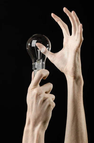 Consumo di energia e risparmio energetico argomento: mano umana che tiene una lampadina su sfondo nero in studio — Foto Stock