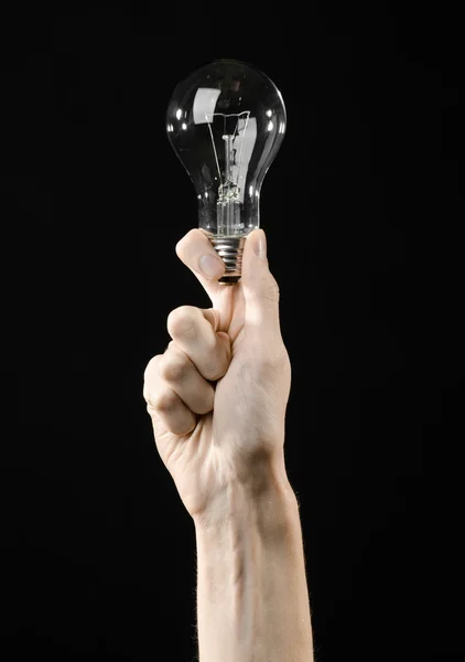 Energy consumption and energy saving topic: human hand holding a light bulb on black background in studio — Stock Photo, Image