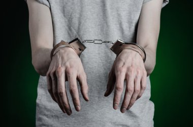 Hapishane ve hüküm giymiş Konu: adam elinde bir gri T-shirt üzerinde kelepçe ve koyu yeşil bir arka plan üzerinde uyuşturucu satıcısı kelepçe koymak Studio, üzerinde kot