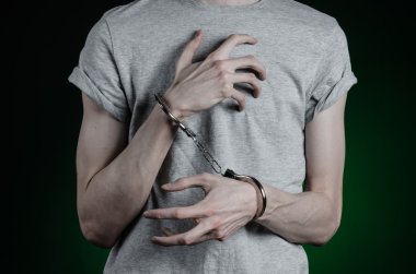 Prison and convicted topic: man with handcuffs on his hands in a gray T-shirt and blue jeans on a dark green background in the studio, put handcuffs on the drug dealer clipart