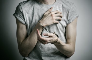 Hapishane ve hüküm giymiş Konu: adam elinde kelepçe tecavüzcü koymak Studio, gri bir arka plan üzerinde gri bir T-shirt üzerinde kelepçe ile