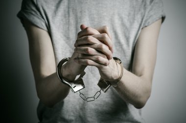 Hapishane ve hüküm giymiş Konu: adam elinde kelepçe tecavüzcü koymak Studio, gri bir arka plan üzerinde gri bir T-shirt üzerinde kelepçe ile