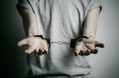 Prison and convicted topic: man with handcuffs on his hands in a gray T-shirt on a gray background in the studio, put handcuffs on rapist clipart